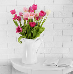 Beautiful tulips in vase on white brick wall background