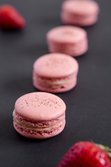 Strawberry macarons on a dark background. These delicate french pastries are made of two meringue cookies and a sweet filling in the center. Light & crisp, these are the perfect luxurious dessert.