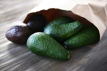 Fresh avocados in paper bag on wooden background
