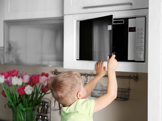 Fototapeta na wymiar Little child playing with a microwave oven in the kitchen
