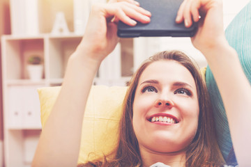 Fototapeta premium Happy young woman reading an e-book on her couch