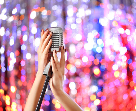 Female hands holding microphone against bright glitter background