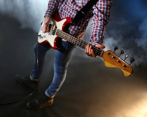 Fototapeta premium Young man playing electric guitar on lighted foggy background
