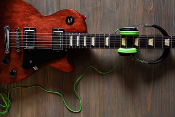 Fototapeta premium Brown electric guitar with headphones on wooden background