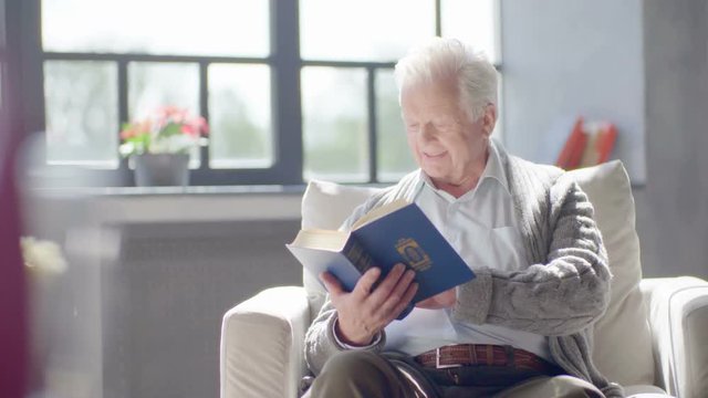 elderly caucasian man reading a book and drinking a delicious tea in a modern apartment