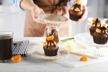 Female baker decorating tasty cupcake with slice of mandarin and chocolate on the table