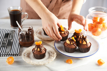 Female baker decorating tasty cupcake with slice of mandarin and chocolate on the table