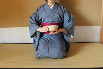 日本の茶室で着物女性がピンクの抹茶の茶碗を両手で持って畳の上に座る
