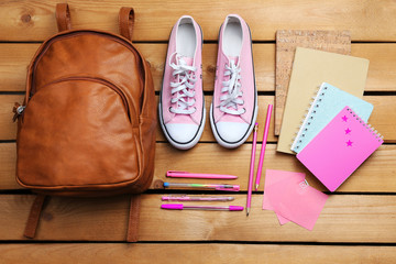 School set with backpack, shoes and supplies on wooden background