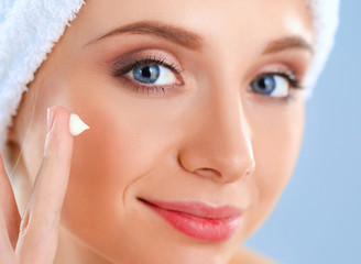 Beautiful young woman applying a creme on her face isolated on gray background