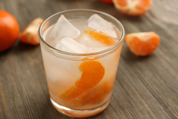 One fresh delicious tangerine cocktail with ice and mandarins on the wooden table, close up
