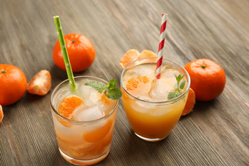 Two fresh delicious tangerine cocktails with ice, mint, straws and mandarins on the wooden table, close up