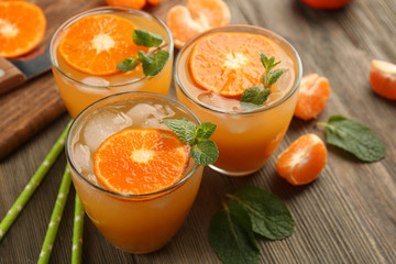Delicious tangerine cocktails with sliced mandarins, ice, garnished with a mint, served on a wooden table, close up