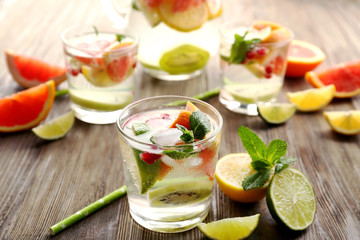 Refreshing cocktails with ice, mint, pomegranate seeds and slices of fruits on wooden background