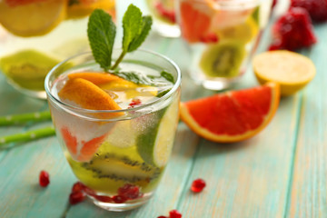 Refreshing cocktail with ice, mint, pomegranate seeds and slices of fruits on blue wooden background