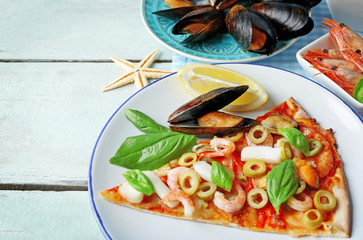 Pizza slices with seafood, red pepper and green olives on wooden table