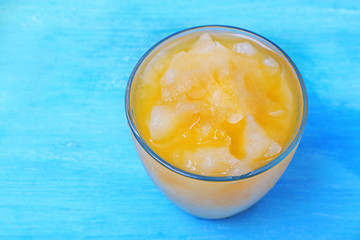 Glass of orange juice with crushed ice on blue wooden table