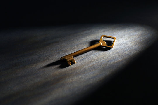 Old key on dark surface with beam of light