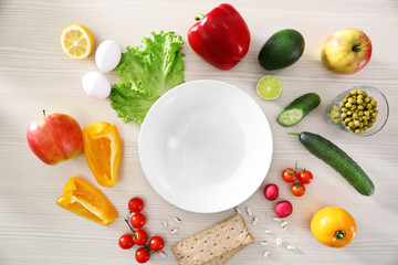 Empty plate and fresh healthy products on wooden table, top view