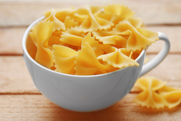 Pasta farfalle in cup on wooden table background