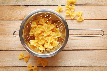 Pasta farfalle in  drainer on wooden table background