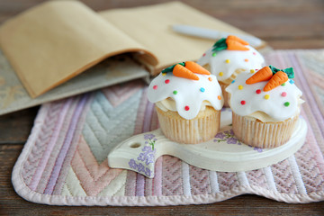 Cupcakes with frosting and decorative carrots on wooden stand