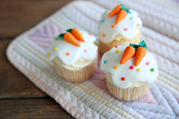 Cupcakes with frosting and decorative carrots on wooden background
