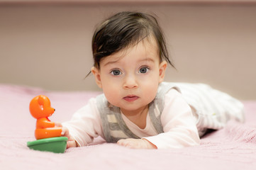 Portrait of little girl close up. Six-month old baby lying on her stomach and plays with a toy. 