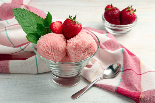 ice cream with strawberries and mint in bowl on napkin on wooden background