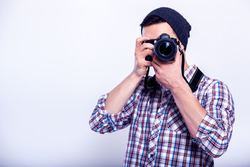 Say cheese! Young man focusing at you with digital camera while standing in studio on gray background