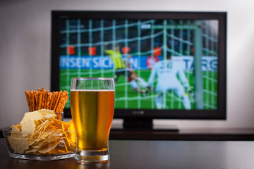 Pint of beer, chips and salty sticks on the tabele in front of televisor show off football..Set of...