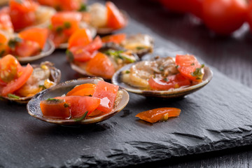 Vongole condite nella loro valva in un piatto di ardesia su un tavolo di legno nero