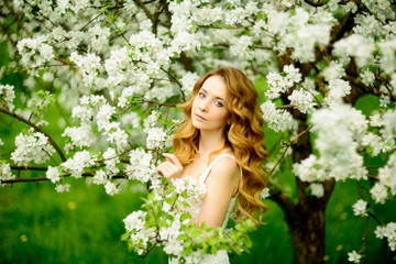 Fototapeta premium Spring beautiful girl, blonde, standing in a blooming Apple orchard .