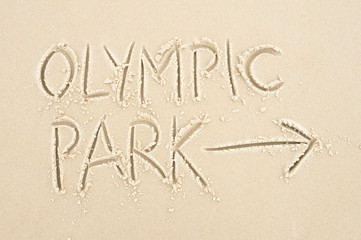 Fototapeta na wymiar Handwritten message with arrow pointing the way to Olympic Park written in smooth sand