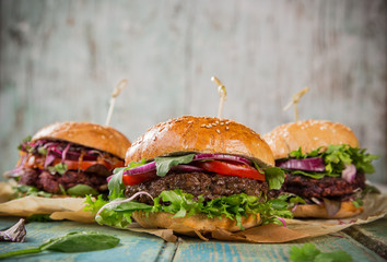 Tasty burgers on wooden table.