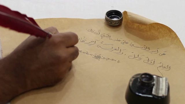 Calligrapher writes Arabic words on an old paper using feather