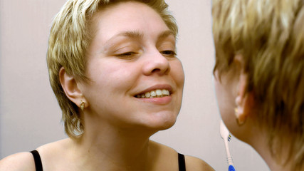 Pretty woman brushing her teeth in front of mirror