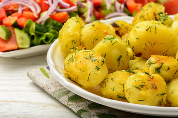Roasted young potatoes with garlic and dill on wooden background.