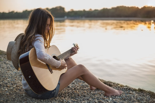 Girl playing guitar while sitting on the beach