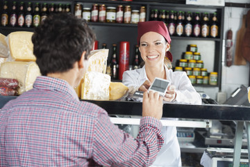 Saleswoman Accepting Payment From Customer In Cheese Shop