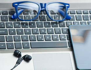 Eyeglasses on laptop keyboard with smartphone and headphones office concept