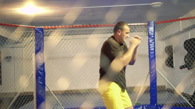 Sportsman training in a boxing cage 4K