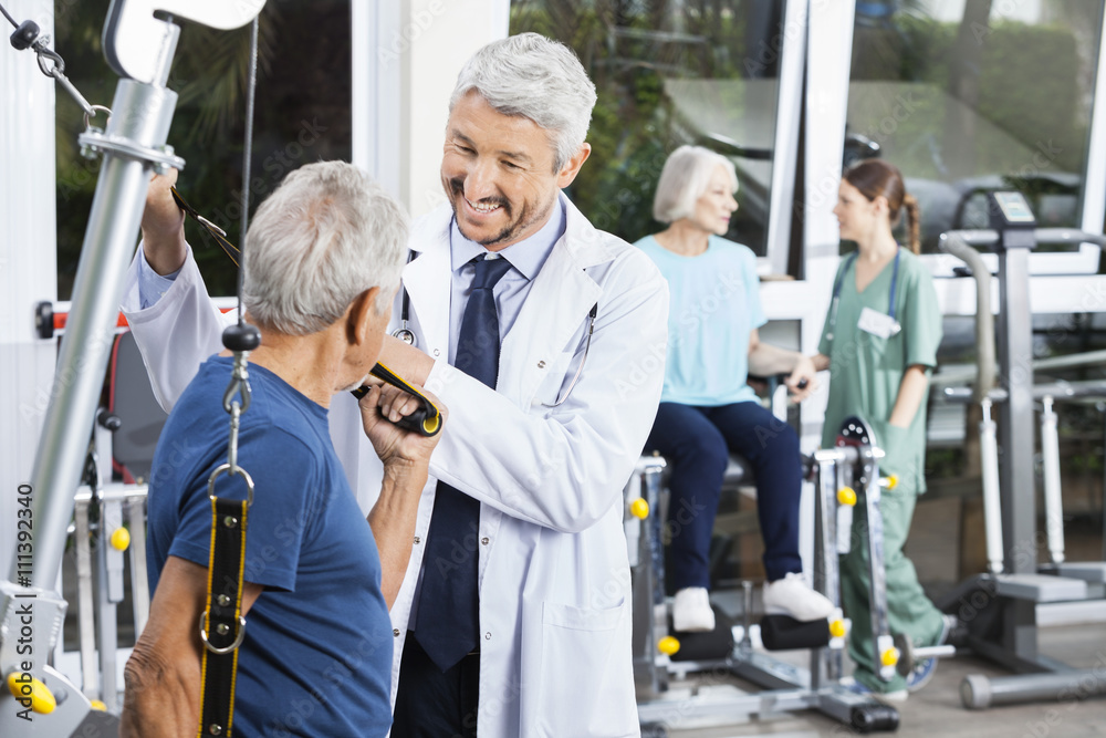 Wall mural Happy Doctor Assisting Senior Man With Resistance Band