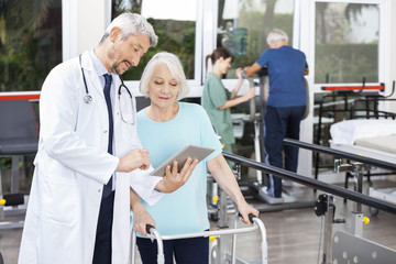 Doctor Showing Reports On Digital Tablet To Woman Using Walker