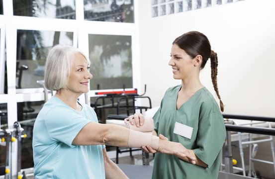 Smiling Female Nurse Putting Crepe Bandage On Senior Woman's Han