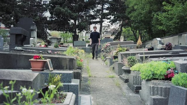 Young Man Walks By Graves In The Cemetery. View of a cemetery with a man walking by the tombs and towards camera
