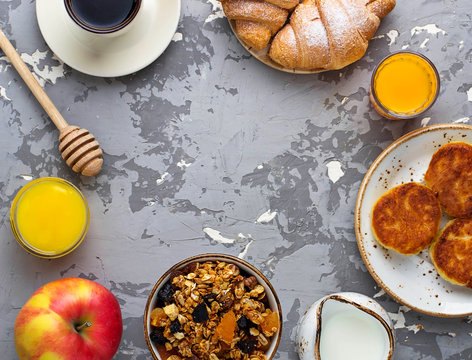 Breakfast table with granola, croissants, apple, coffee, juice.