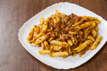 pasta penne with stew meat sauce in a plate on wooden table