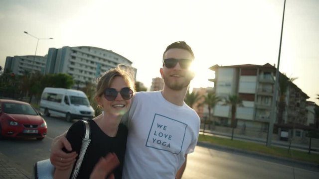 young couple walking along the road and waving hands to camera slow motion