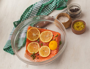 Fillet of red fish with lemon slices and spices in a glass bowl